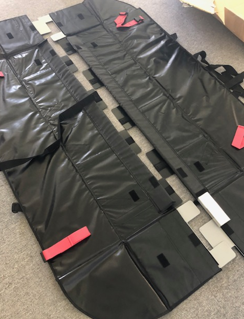 Two black storage mats with straps and velcro fasteners laid flat on a gray surface.