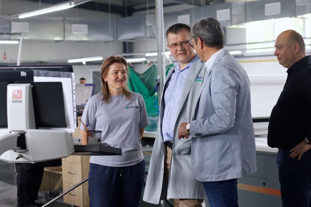 A group of four professionals engaging in a discussion in a modern workshop setting, with technology and machines in the background.