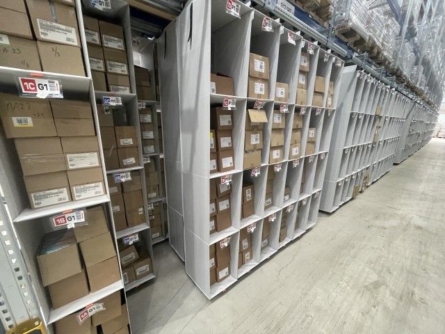 Warehouse storage area with shelves filled with labeled boxes and packages.