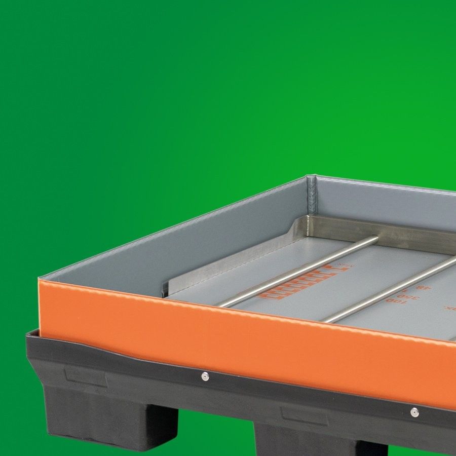 A close-up of a plastic tray with an orange border and a gray interior, featuring metal tracks inside, set against a green background.