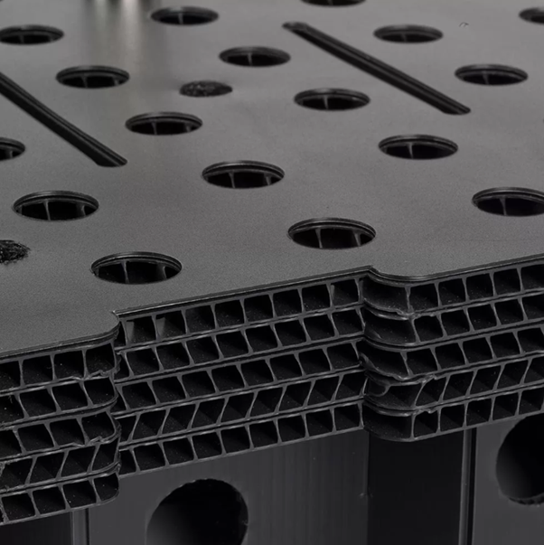 Close-up of a black, layered plastic structure with multiple round and rectangular holes, showcasing a textured surface.