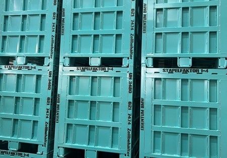 Stacked turquoise pallets with text printed on the sides, including "STAPLEFAKTOR" and other numbers and labels.