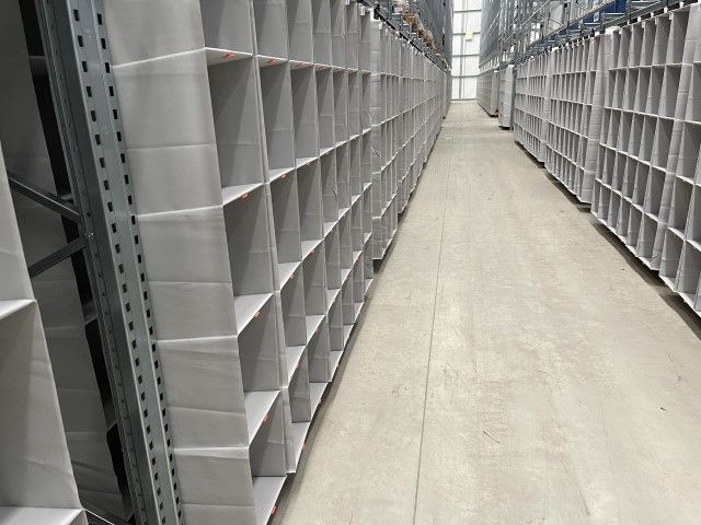 Rows of empty shelving units in a large warehouse, with a wide aisle in between.