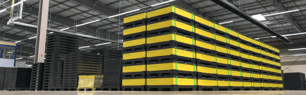Warehouse interior with stacked black pallets and yellow containers.