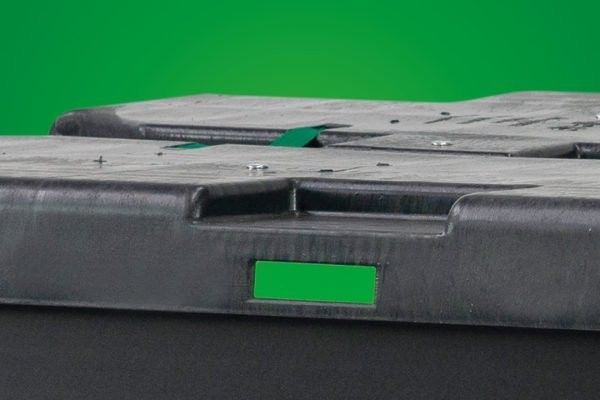 Close-up of a black plastic container lid with a handle and a green background.