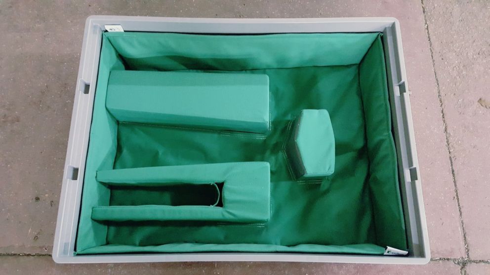 A top-down view of a rectangular box with a green fabric lining and several foam inserts in varying shapes and sizes arranged inside.
