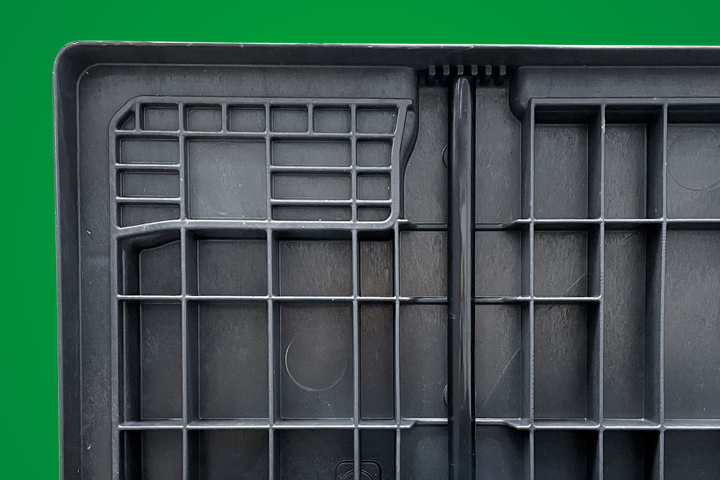 Black plastic storage container lid with grid pattern and central handle, set against a green background.