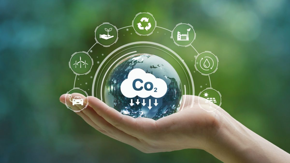 A hand holding a transparent globe with icons representing eco-friendly practices and the reduction of carbon dioxide emissions.