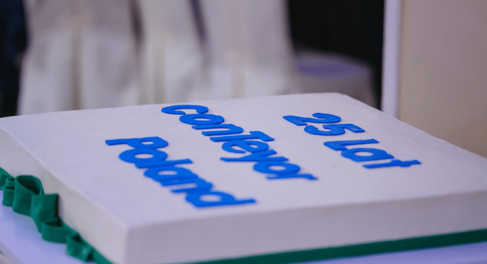 A decorated cake with the text "25 Lat Conveyor Poland" in blue letters on top.