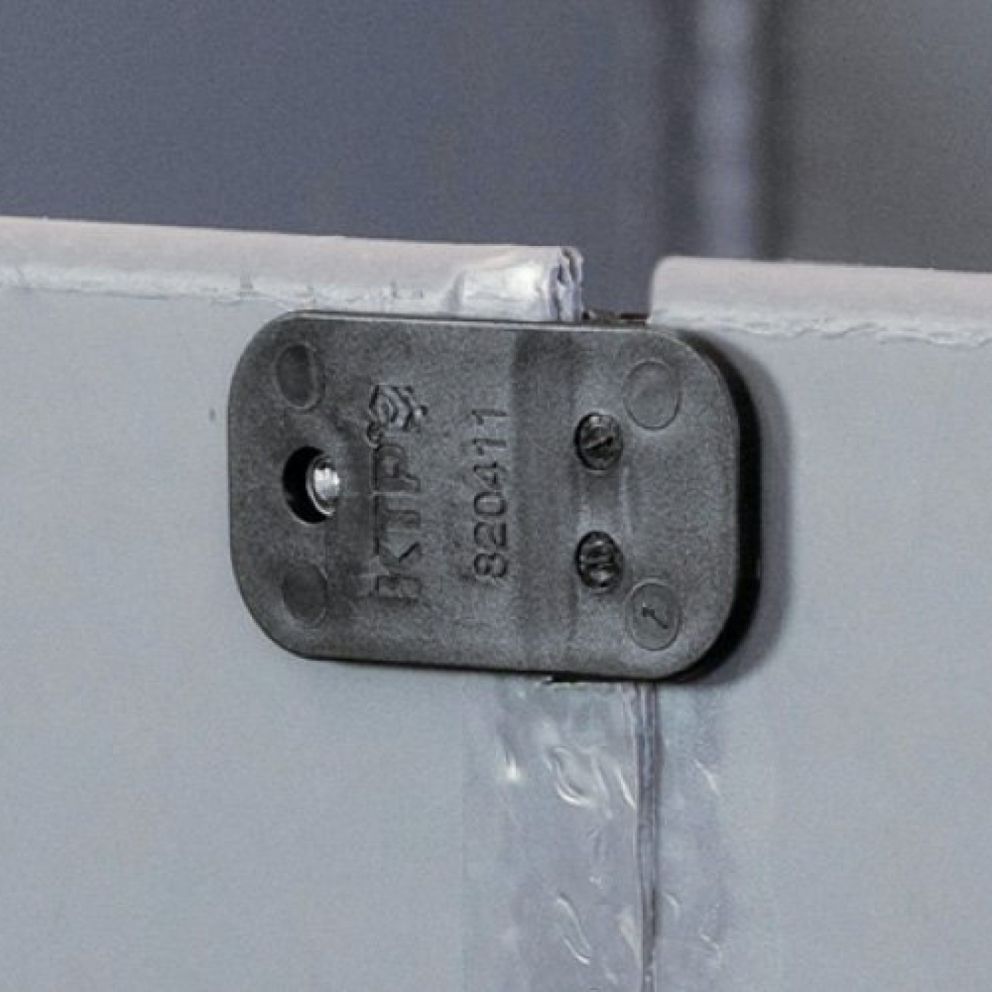 Close-up of a black mounting clip attached to a metal surface, with visible screws and engraved markings.
