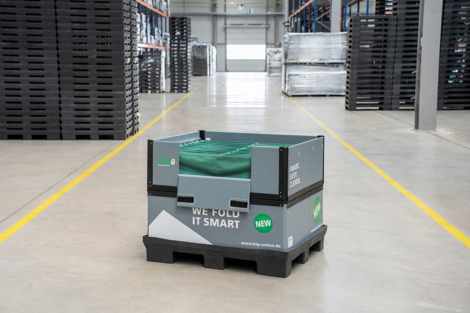 A foldable storage box on a pallet, located in a warehouse with rows of stacked pallets in the background.