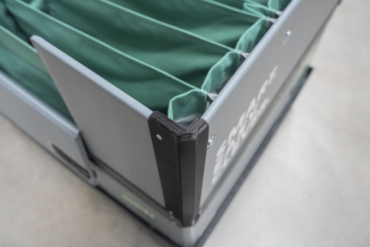 Close-up of a gray storage container with a black corner piece and green fabric dividers inside.
