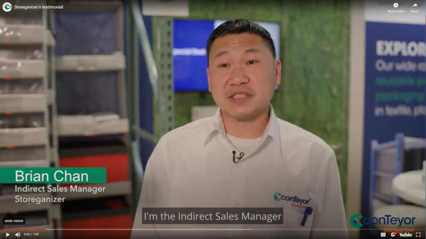 A man with short hair is speaking in an office setting, wearing a white shirt with a company logo. He introduces himself as the Indirect Sales Manager for Storeganizer. In the background, there are storage shelves and a blue display with company branding.