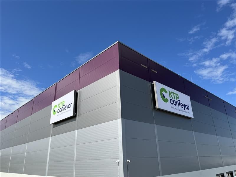 A modern building with a purple and gray exterior featuring a sign that reads "KTP conveyor" against a clear blue sky.