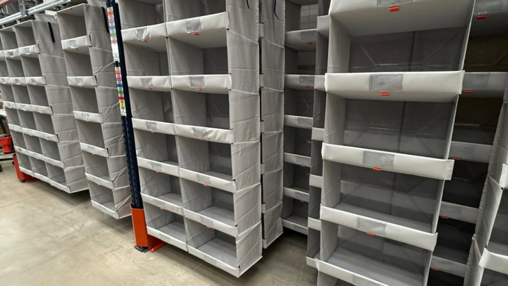 A row of gray fabric shelves displayed in a warehouse or retail setting, with several empty compartments.