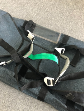 A dark fabric bag with adjustable straps and a transparent pocket on top, laid on a gray surface.