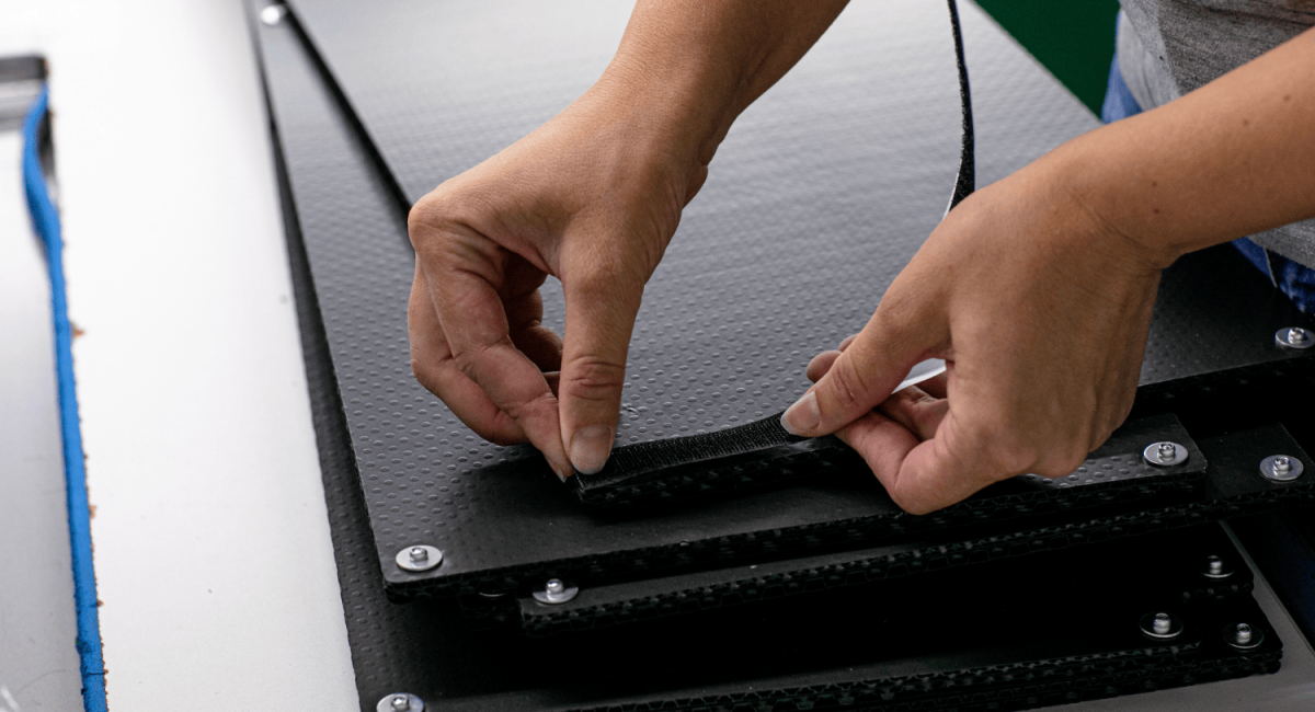 A person using their hands to attach a strap to a textured black surface in a workspace.