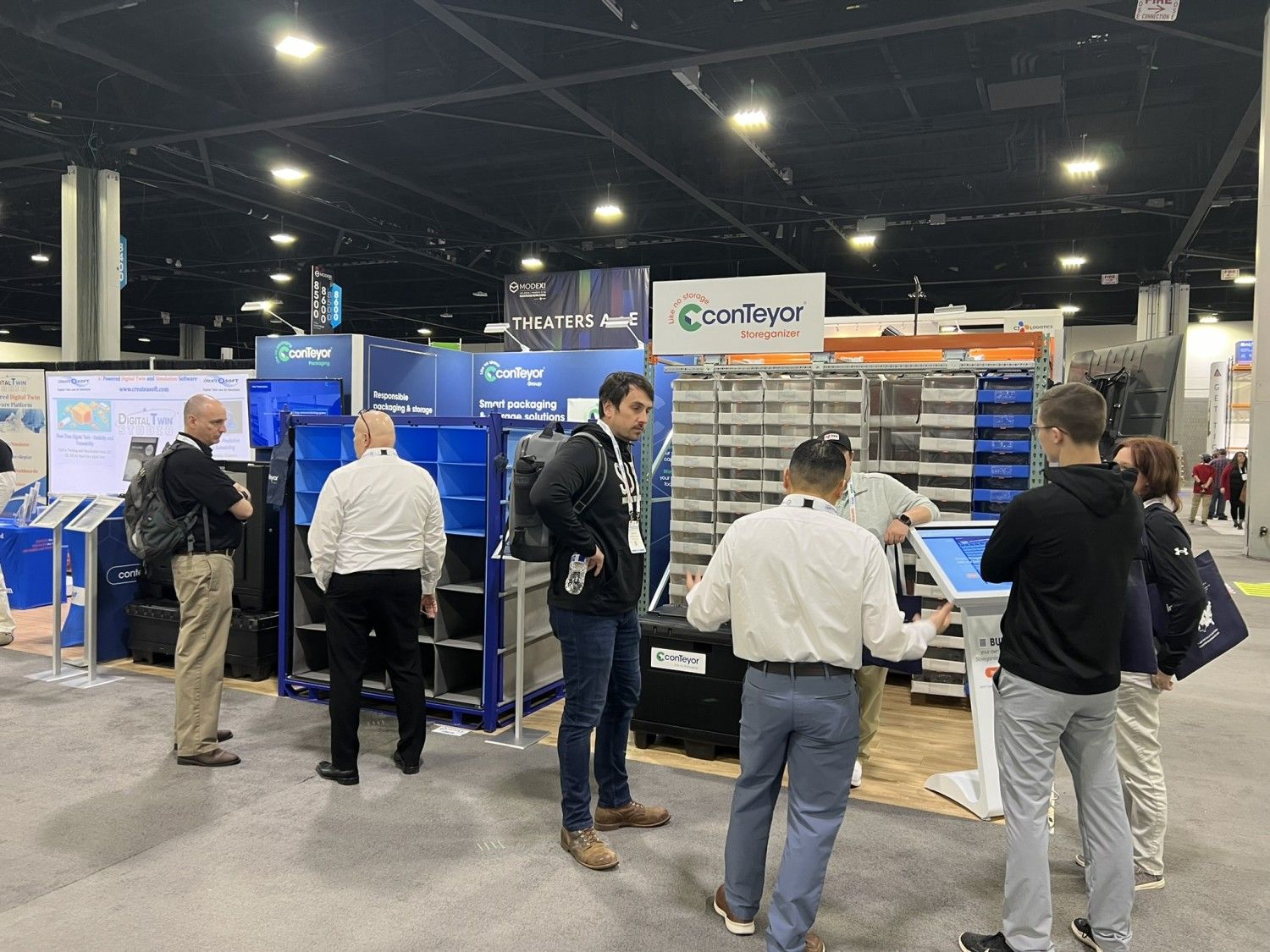 A trade show booth with several attendees discussing products, featuring blue storage containers and informational displays.