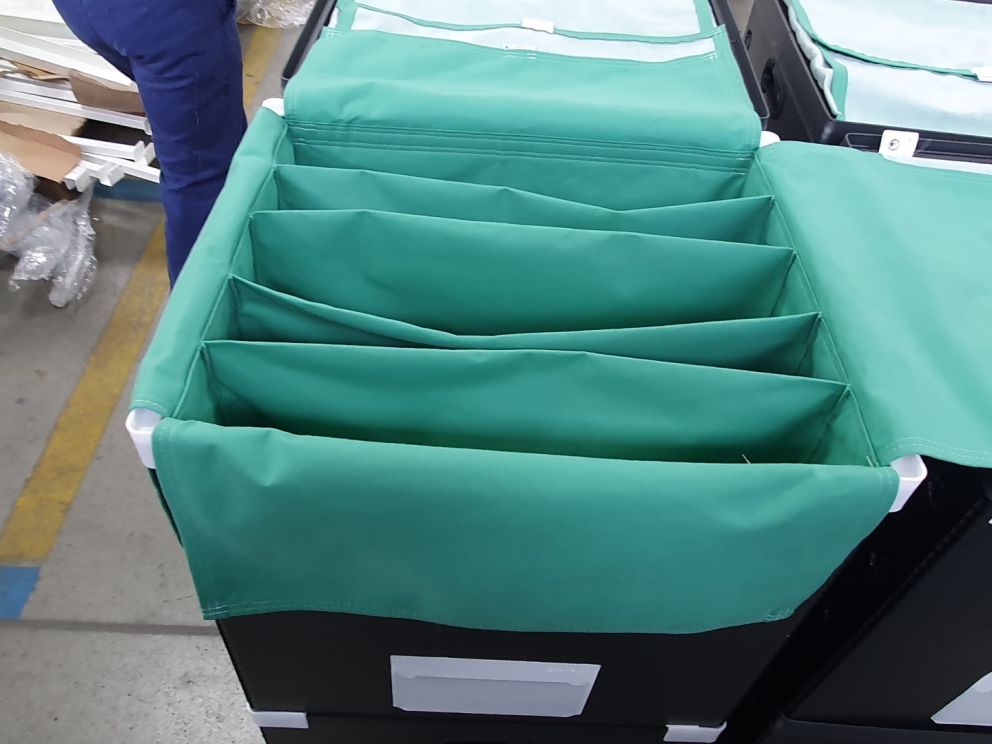 Green fabric organizers with multiple compartments inside a black storage unit, partially visible in a workspace.